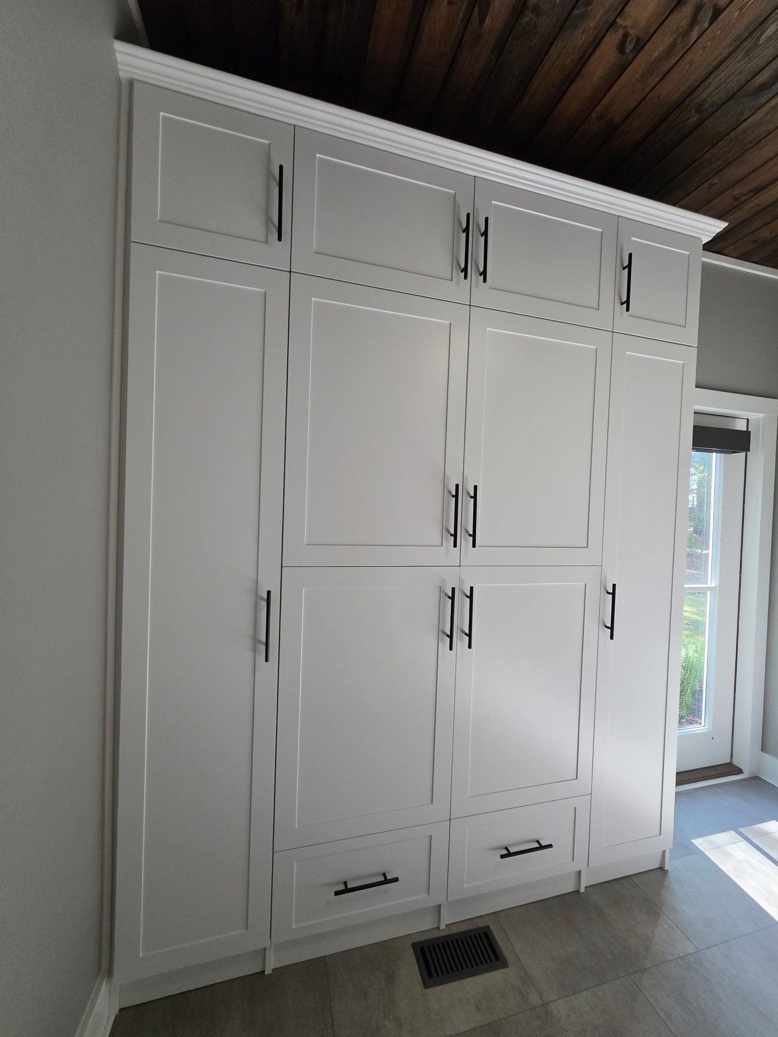 White built-in cabinets with multiple handles and a wooden ceiling above.