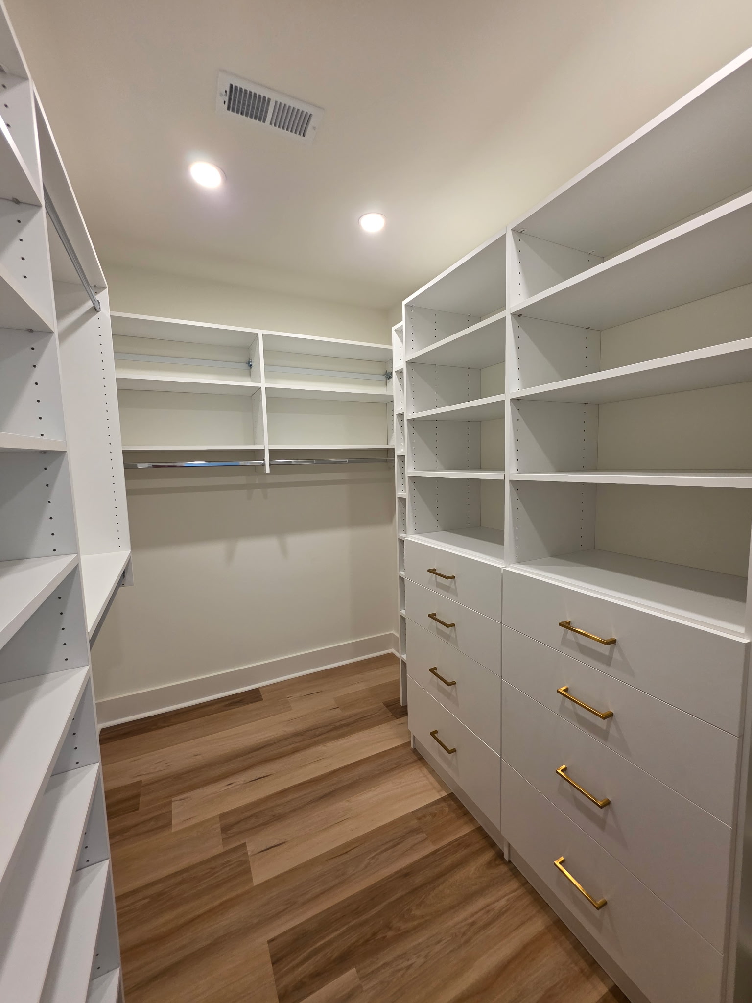 Spacious walk-in closet with white shelves and wooden floor.