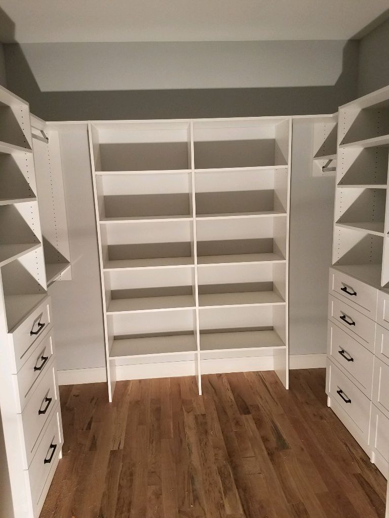 A spacious walk-in closet with white shelving and drawers.