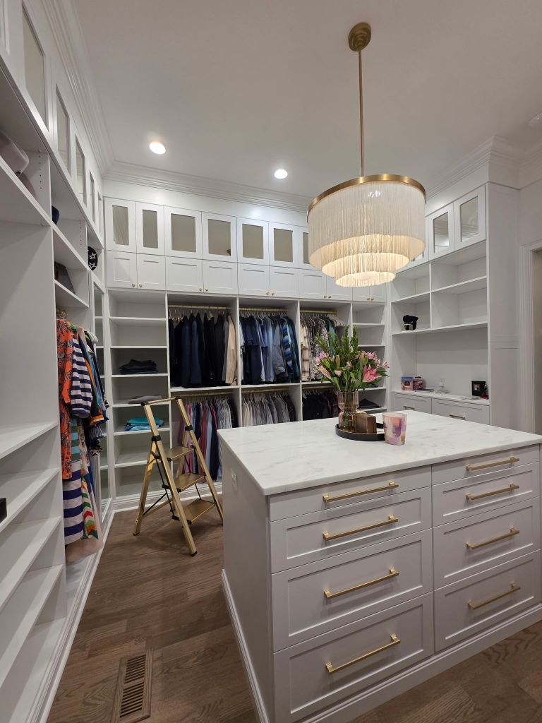Spacious, modern walk-in closet with white cabinetry and chandelier.