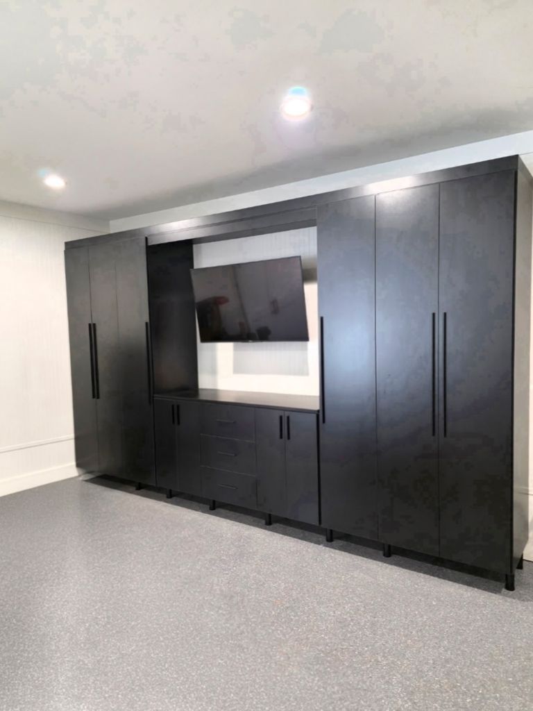 Modern black storage cabinets with an open TV space in a clean room.