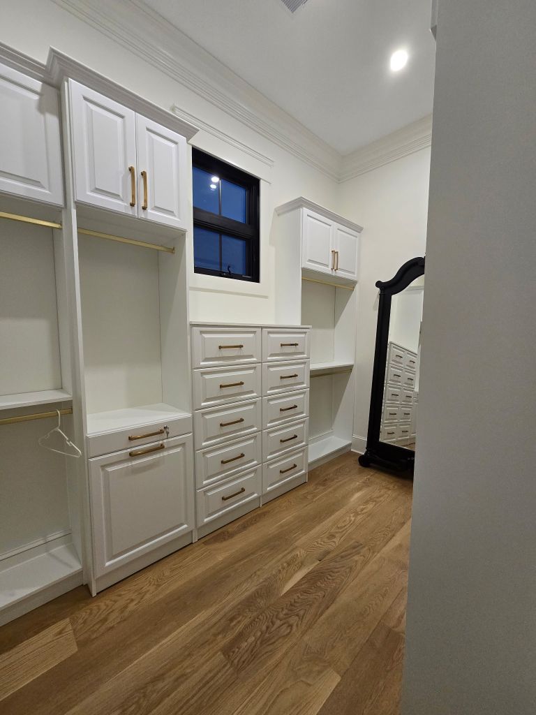 A modern walk-in closet with white cabinetry and a full-length mirror.