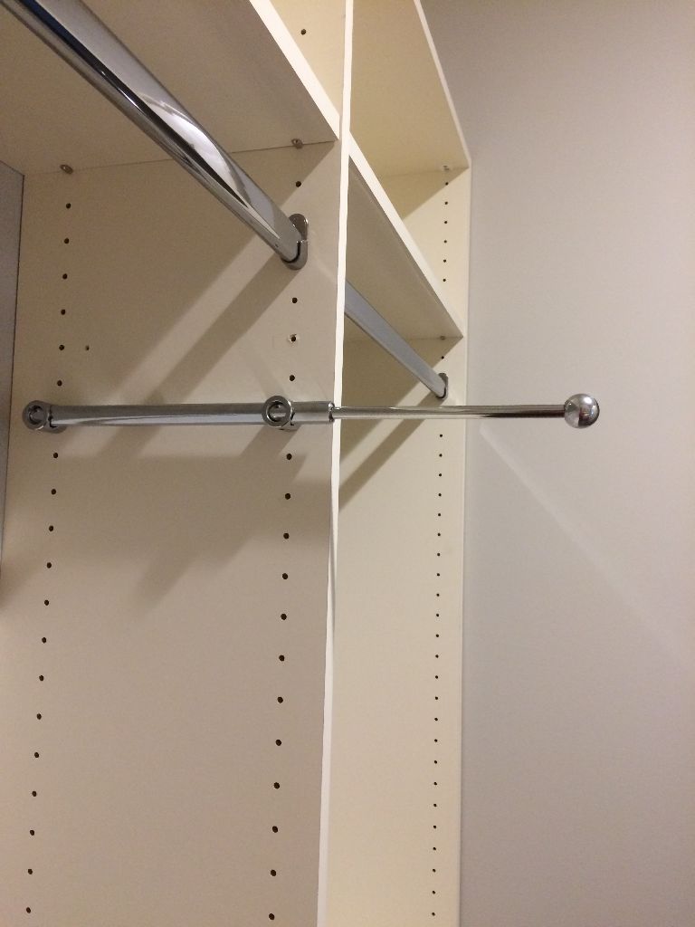 Adjustable metal closet rod installed between shelves.