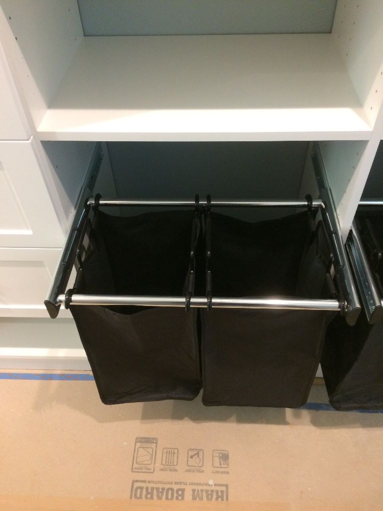 Double black laundry hampers built into a white cabinet.