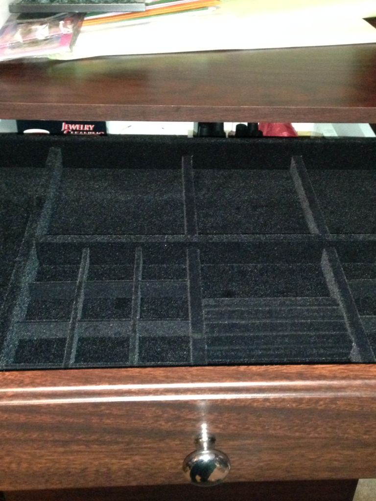 Empty black velvet jewelry organizer with multiple compartments on a wooden surface.