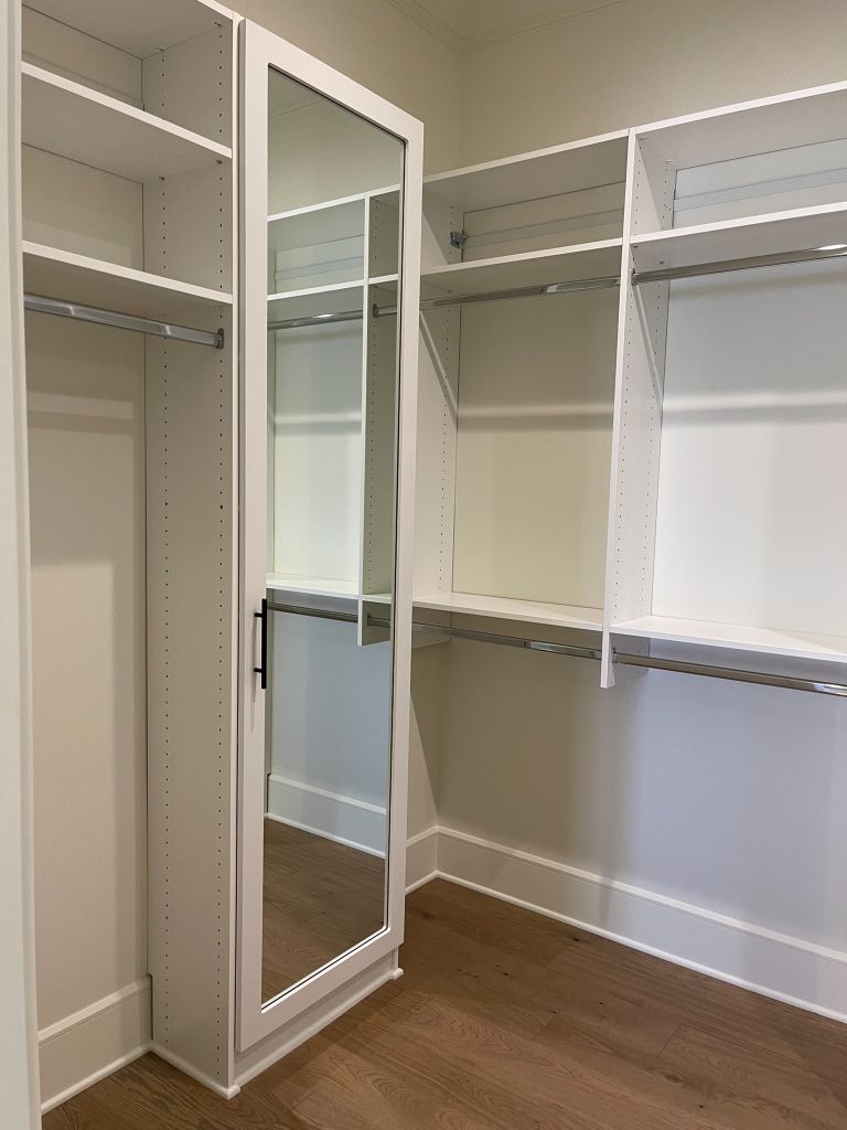 Empty walk-in closet with white shelves and a mirrored door.