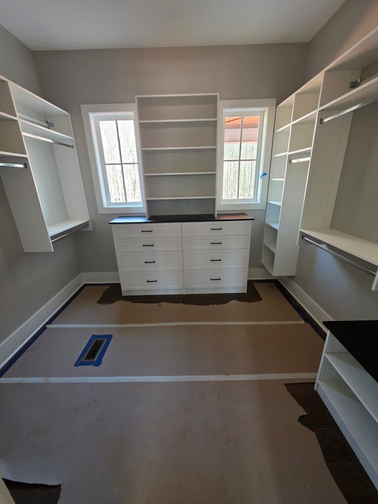 Empty walk-in closet with white shelving and drawers under natural light.