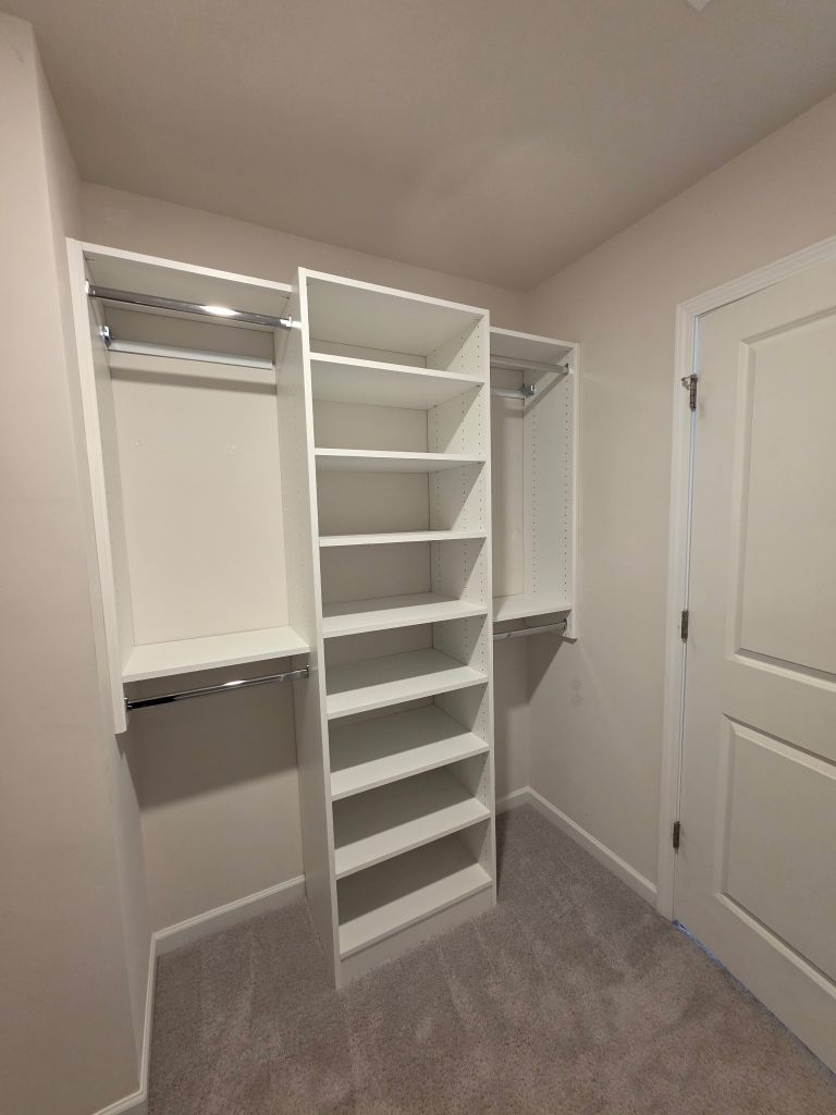 A spacious white walk-in closet with shelves and hanging rods.