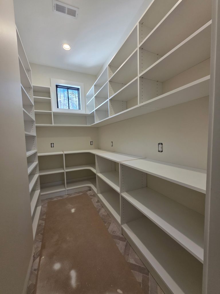 Empty walk-in pantry with white shelves and window.