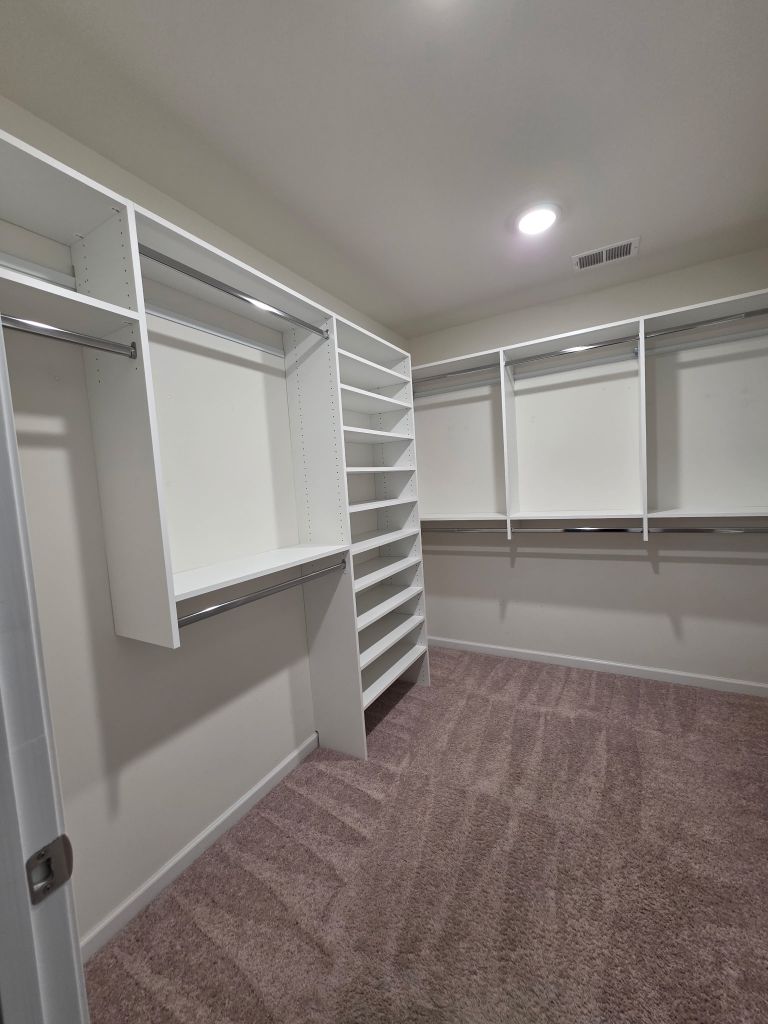 Spacious empty walk-in closet with white shelves and hanging rods.