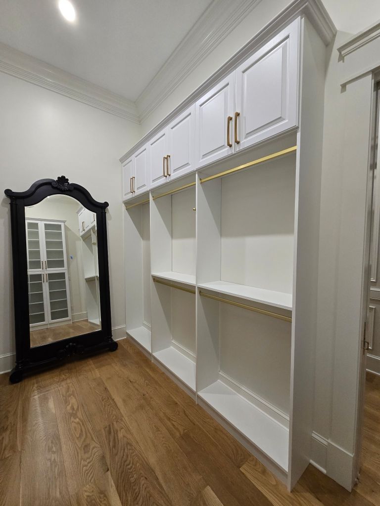 White built-in bookshelves with a large ornate black-framed mirror on wooden floor.