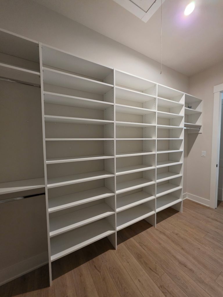 Empty white shelving unit in a spacious room with wooden flooring.