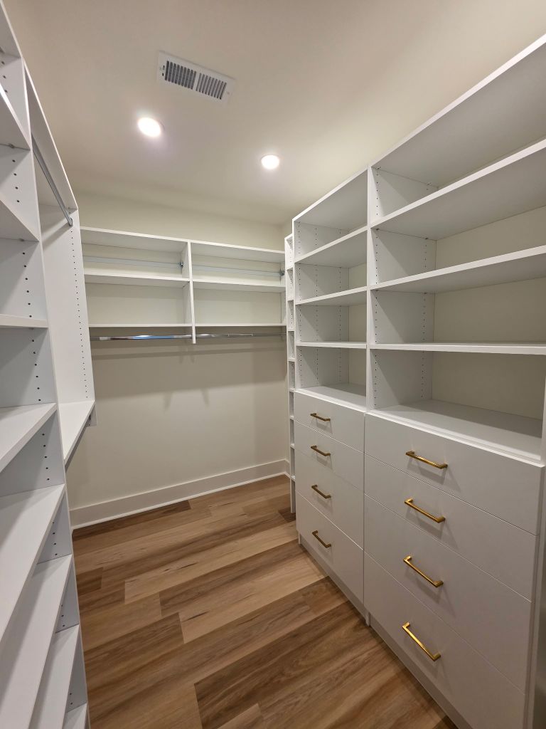 Spacious walk-in closet with white shelving and wooden floors.