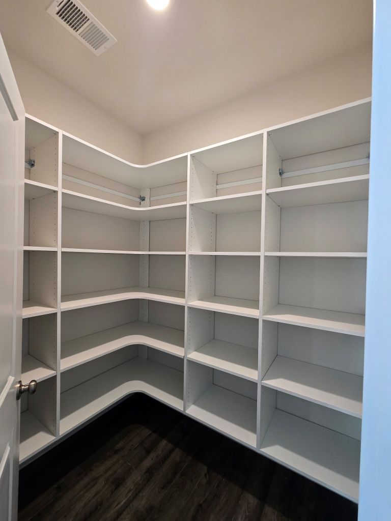 Empty corner pantry with white shelves and dark floor.