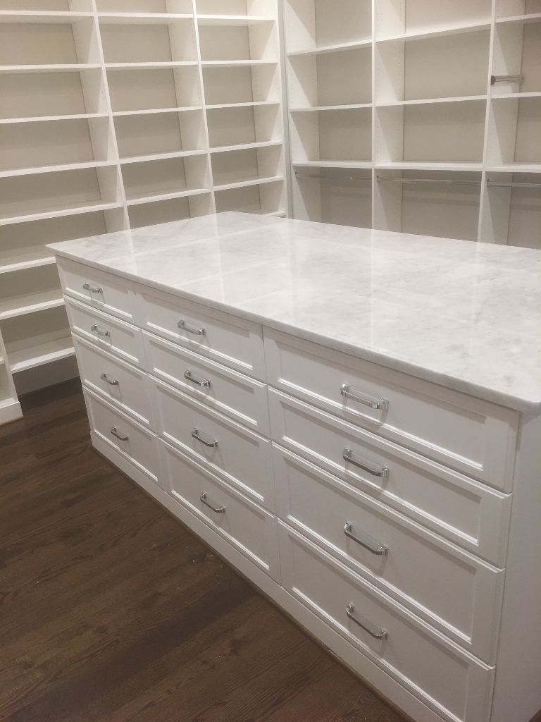 White kitchen island with marble countertop and multiple drawers.