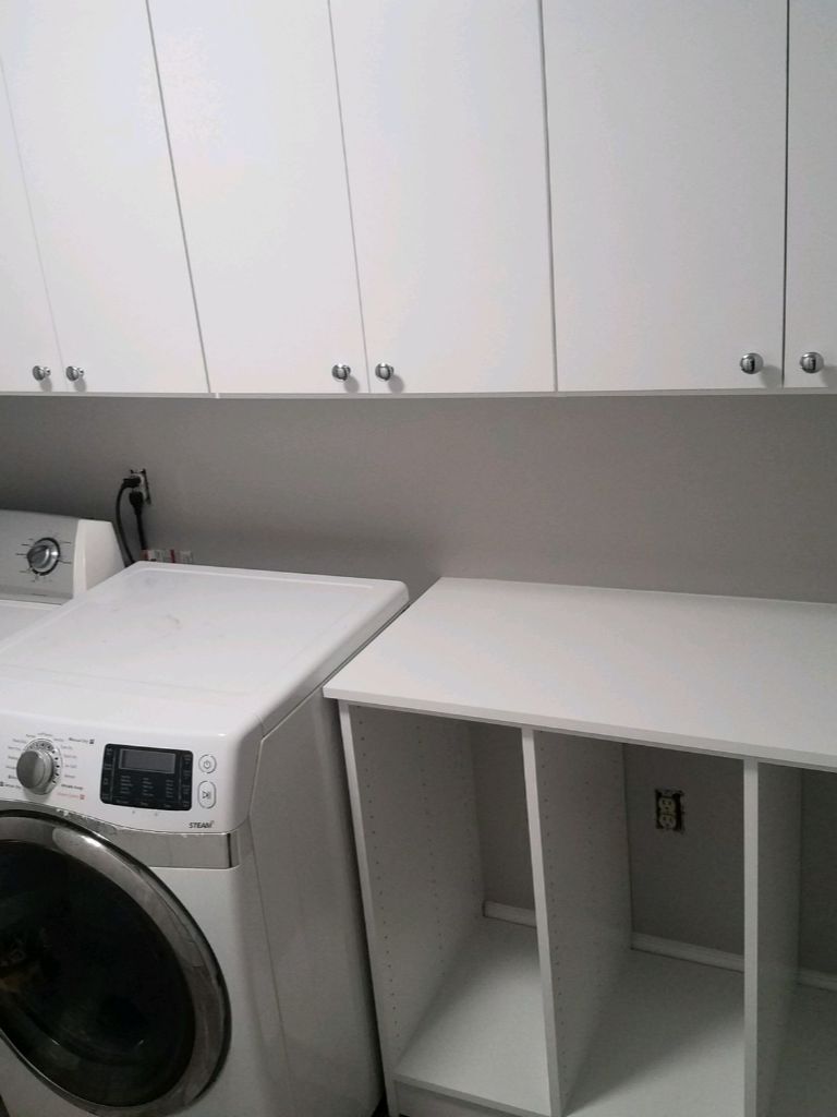 Compact laundry area with washer and countertop under white cabinets.
