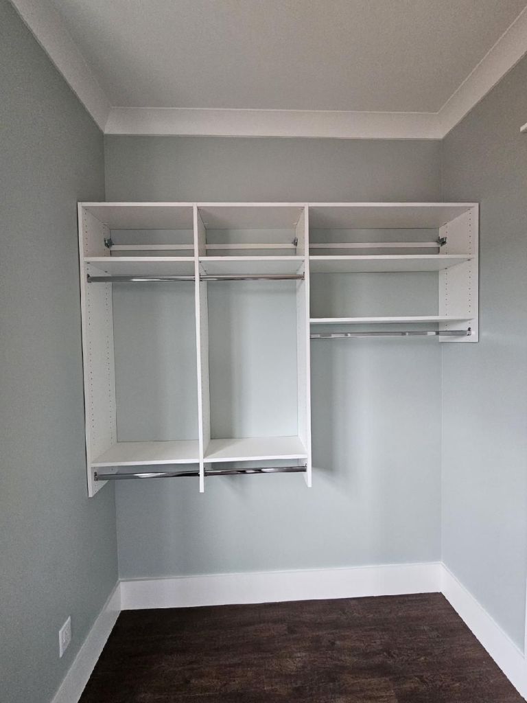 Empty white wall-mounted closet organizer with shelves and hanging rods.