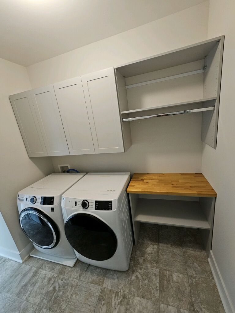 Modern laundry room with washer, dryer, cabinets, and wooden countertop.